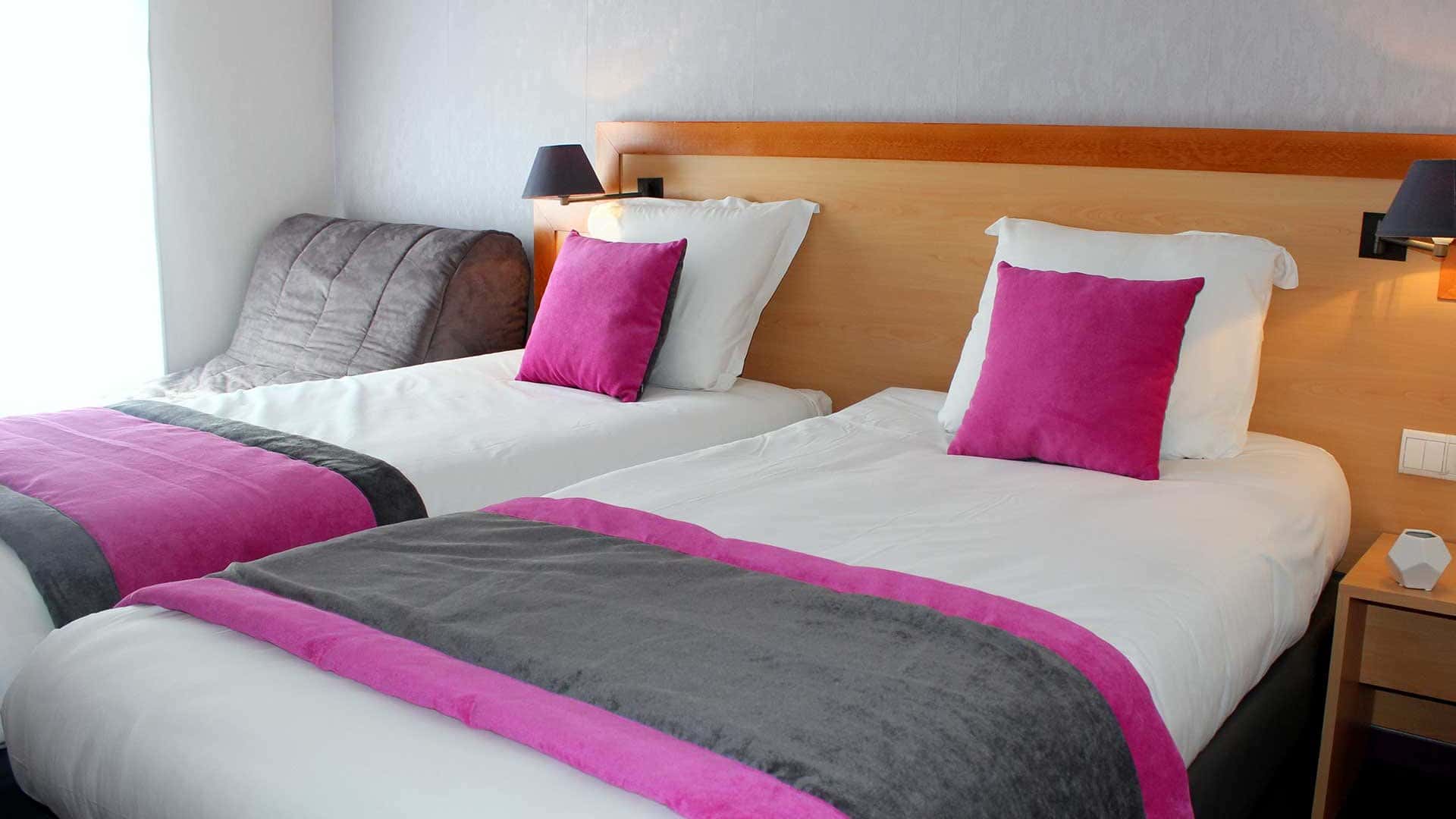 Chambre d'hôtel avec deux lits simples munis de couettes blanches, dessus-de-lit gris avec bordures violettes et coussins violets.