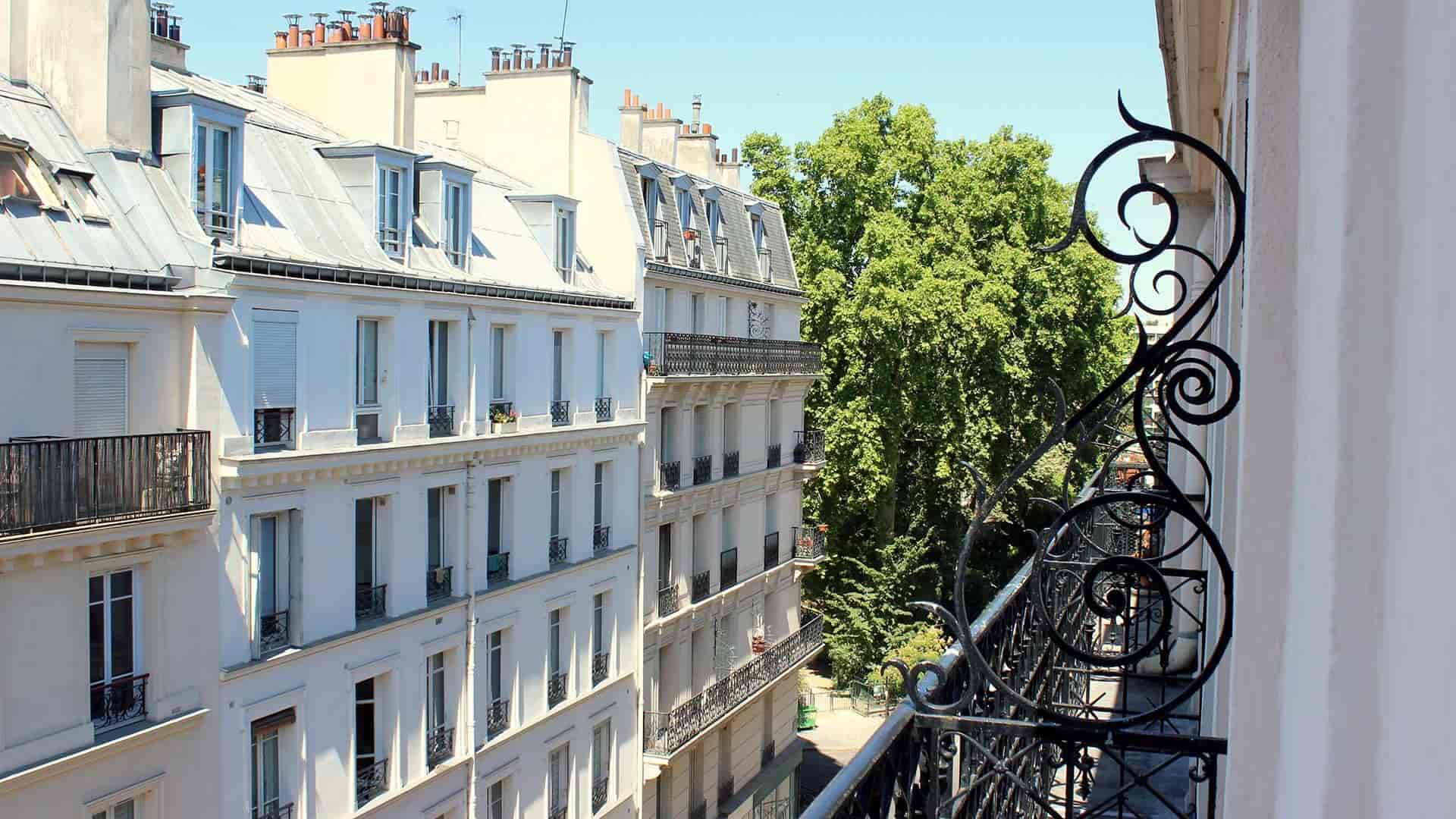 Vue sur les balcons en fer forgé et les façades des immeubles parisiens sous un ciel bleu clair.