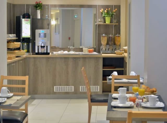 Salle de petit-déjeuner avec tables dressées, boissons et distributeurs de céréales sur un comptoir en bois clair.